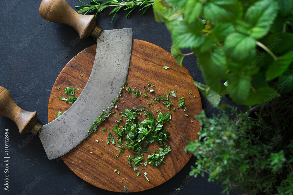 © Ina - Aromatic herbs chopped with mezzaluna knife on wooden cutting board