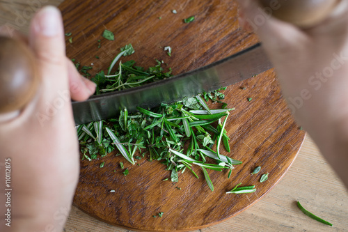 Chopping aromatic herbs with italian mezzaluna knife. Selective focus. photo