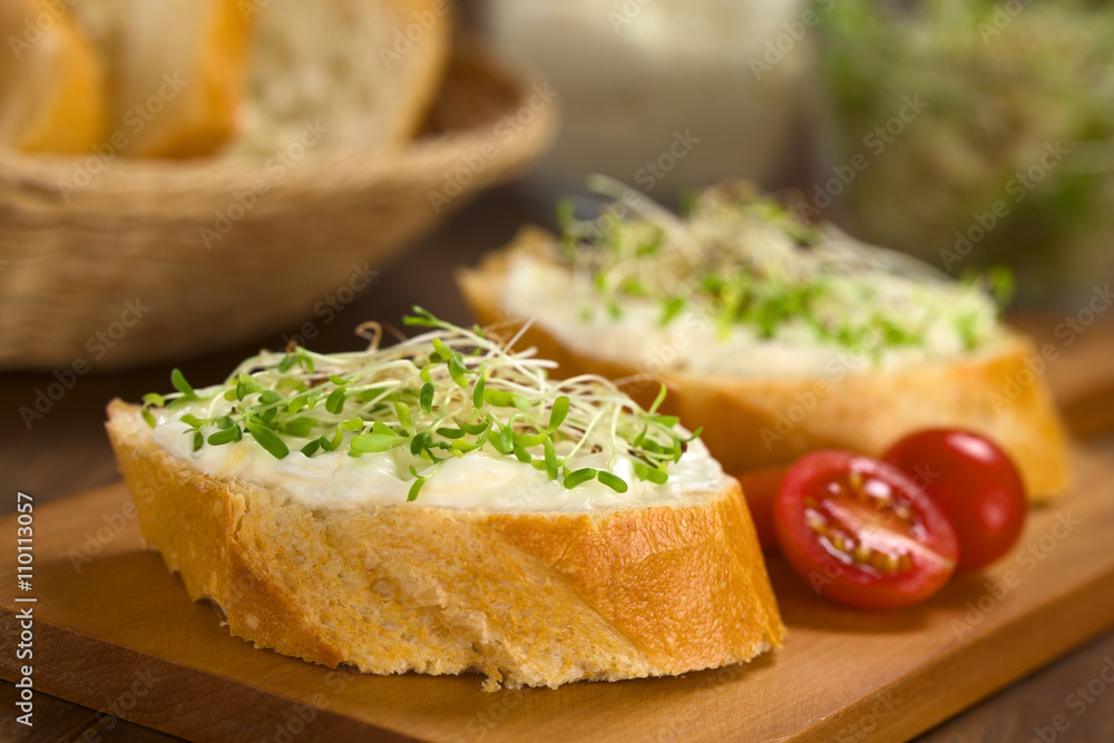 Baguette belegt mit Frischkäse und Luzerne-Sprossen auf Holzbrett (Selektiver Fokus, Fokus auf den vorderen Teil des Frischkäse auf dem ersten belegten Brot)