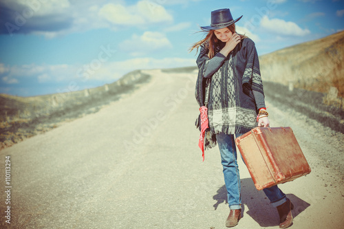 Grl in poncho with suitcase stands on road