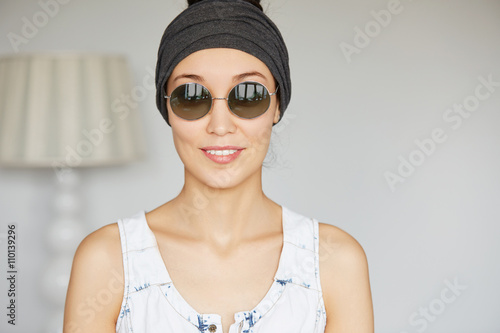 Fashionable student girl wearing round sunglasses going for a walk with her friends after classes at university. Stylish female looking and smiling at the camera. Human face expressions and emotions