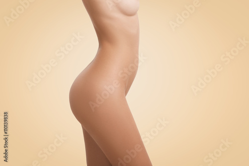 Side cropped view of young female body with naked torso posing isolated against blank wall background with copy space for your text or advertising concept. Portrait of woman with perfect tanned skin