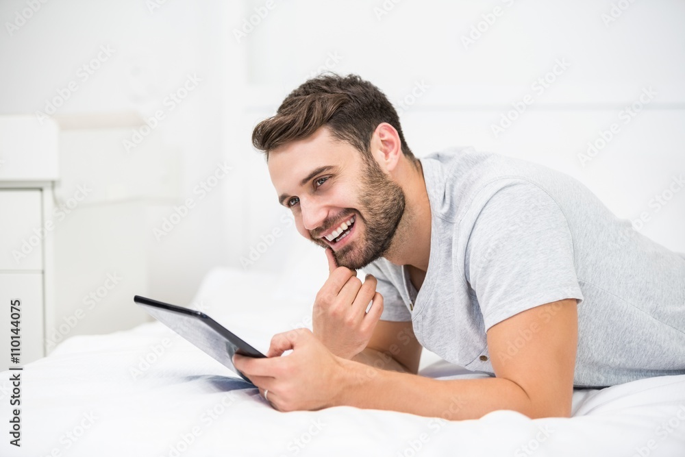 Man smiling while using digital tablet on bed Man smiling while using digital tablet on bed