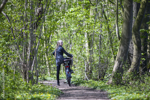 young blond girl with bicycle amongst fresh green spring foliage