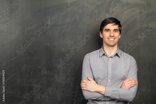 Portrait of young happy smiling teacher man standing near chalkboard background