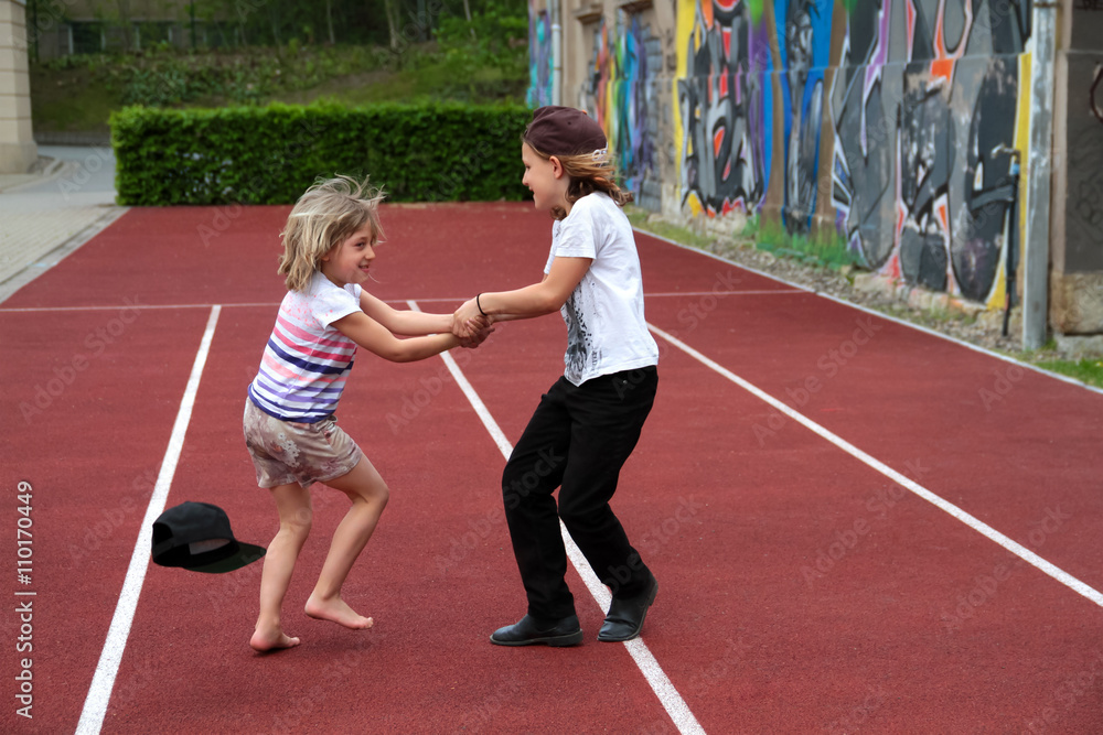 Zwei fröhliche Kinder spielen, drehen sich auf der Laufbahn Sportplatz Schule