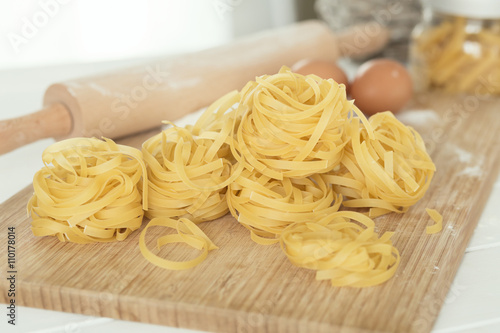 Uncooked dried tagliatelle over cutting board with flour and eggs