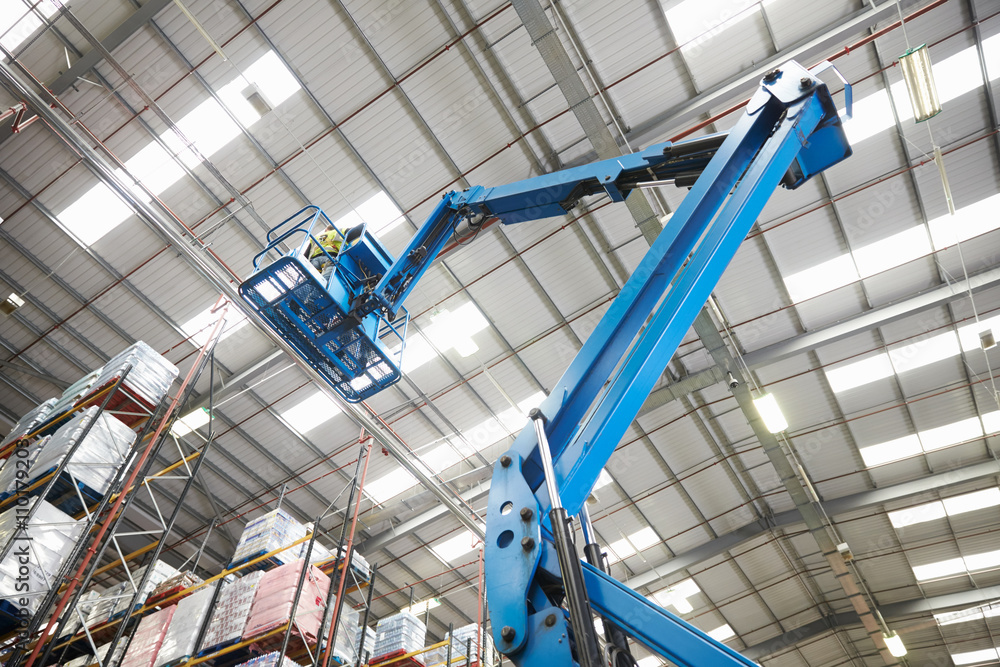 Moving stock in a warehouse with a cherry picker, low angle - obrazy, fototapety, plakaty 