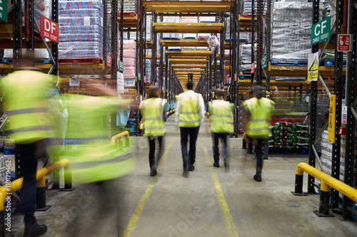 Staff in reflective vests walking in a warehouse, back view photo