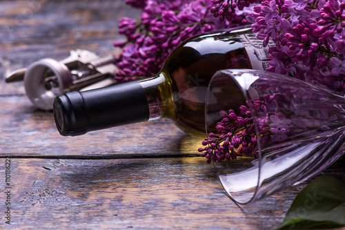 Bottle of white wine with lilac flowers on wooden background