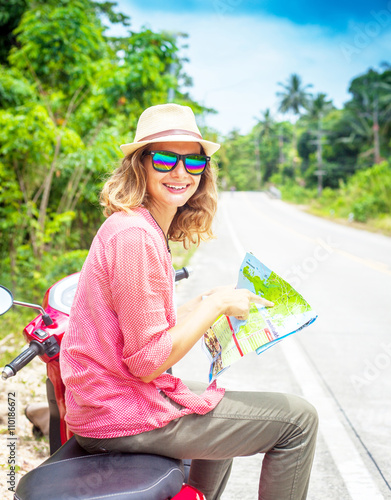 Beautiful young woman with map in hand and a motorbike on the ro