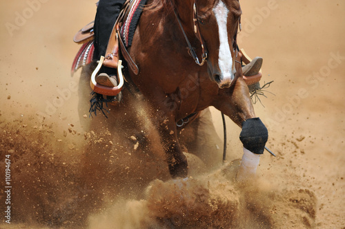 A close up view of a rider sliding the horse in the dirt