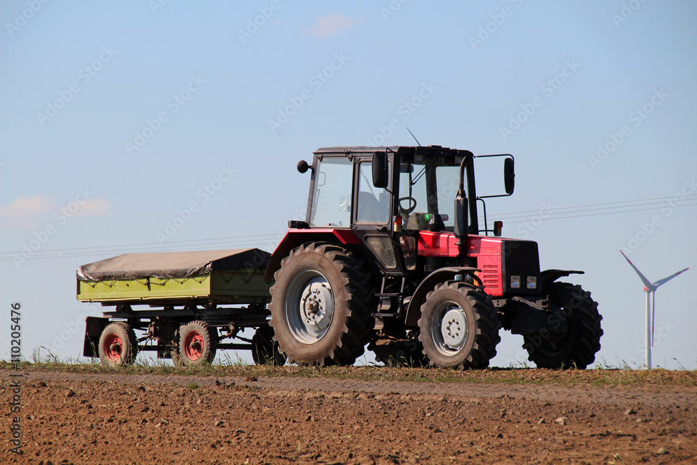 Red tractor with green trailer on a field Red tractor with green trailer on a field