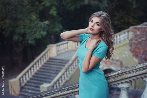 Outdoor lifestyle portrait of pretty young girl, wearing in blue dress on urban background. Creative color toned image.