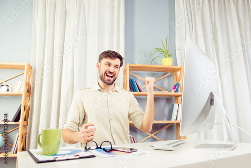 Cheerful happy young  man triumphing with raised hands photo