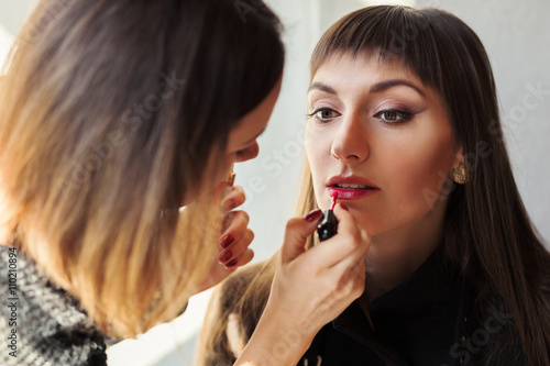 Make-up artist applying lipstick with brush on model lips
