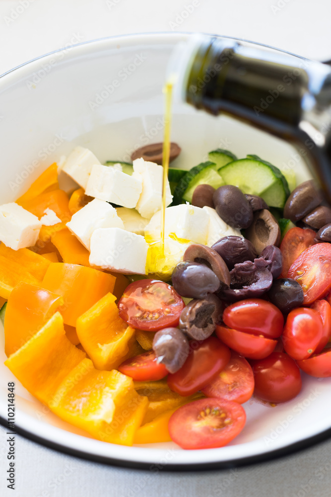 Olive oil being poured into bowl with ingredients for greek salad. Selective focus. Olive oil being poured into bowl with ingredients for greek salad. Selective focus.