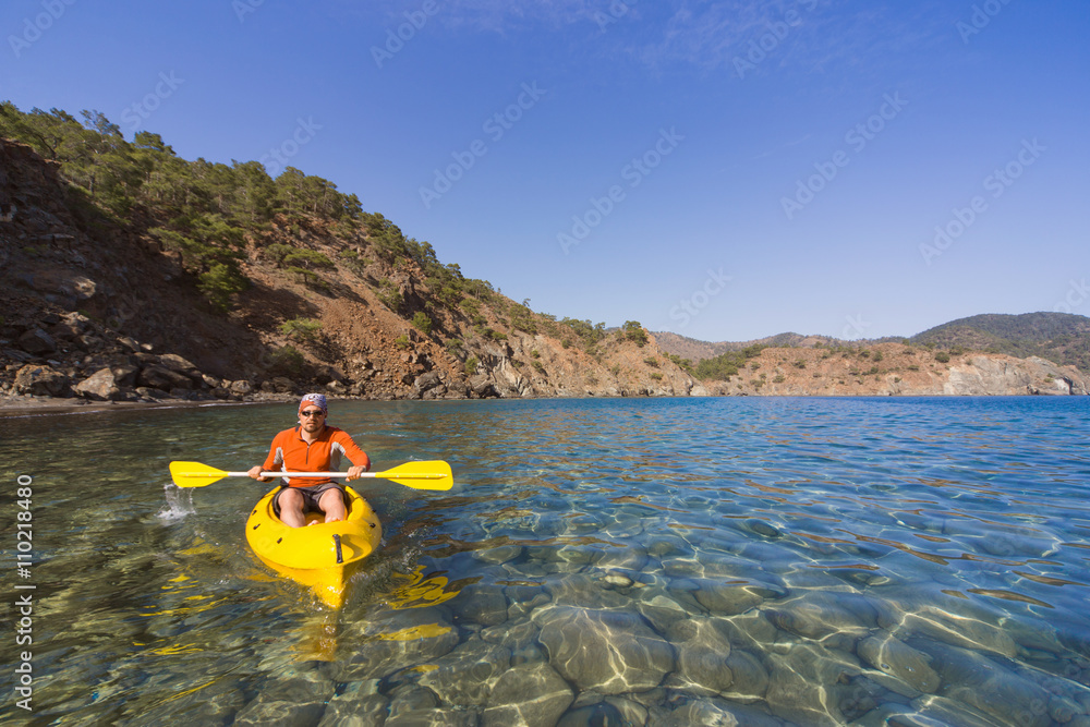 A man traveling by canoe along the coast in the summer.