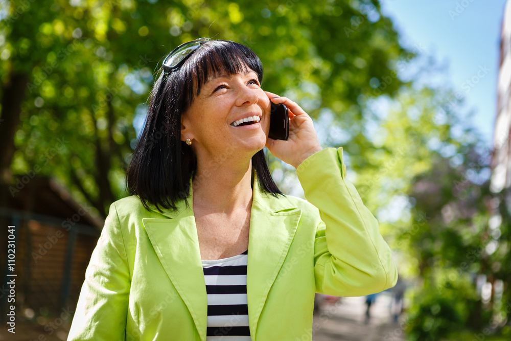 Woman with white smile speaking by mobile cell phone in outdoor. Happy Lady Dressed in a green jacket and have spring-summer mood Woman with white smile speaking by mobile cell phone in outdoor. Happy Lady Dressed in a green jacket and have spring-summer mood