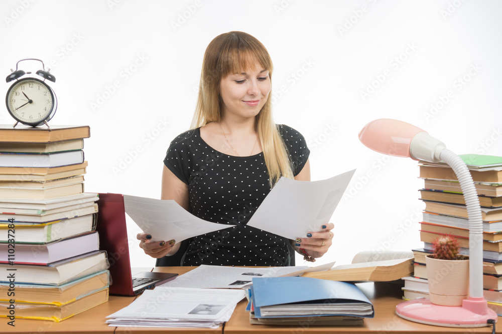 Joyful girl behind a desk littered with books, looking at the paper in his hands Joyful girl behind a desk littered with books, looking at the paper in his hands