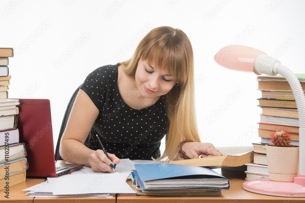 A student at a table littered with books in the library happily writes synopsis A student at a table littered with books in the library happily writes synopsis