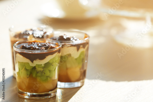 Fruits in glasses with whipped cream and chocolate syrup.