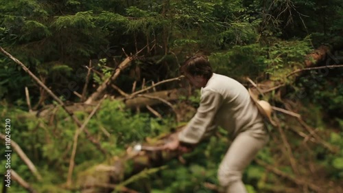 Young countryman woodcutter in traditional ukrainain clothes chopping wood in the green forest of Carpathian mountains photo