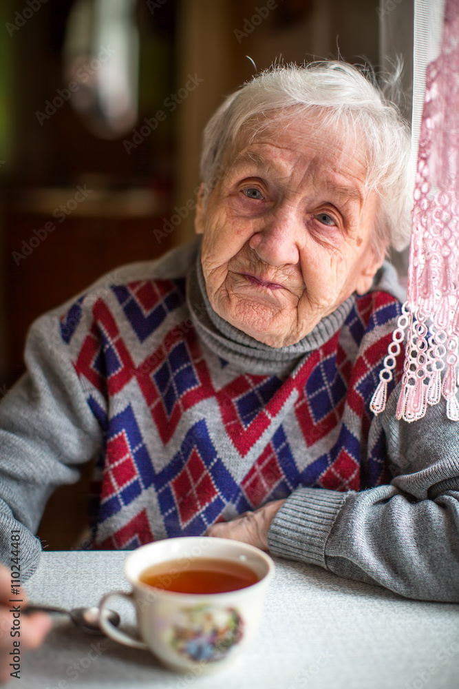 An old woman sitting in the kitchen drinking tea. An old woman sitting in the kitchen drinking tea.
