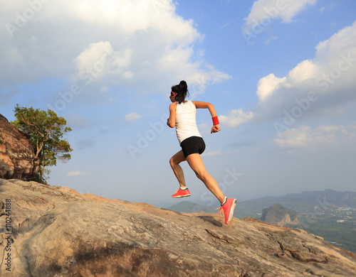 young woman trail runner running on mountain peak