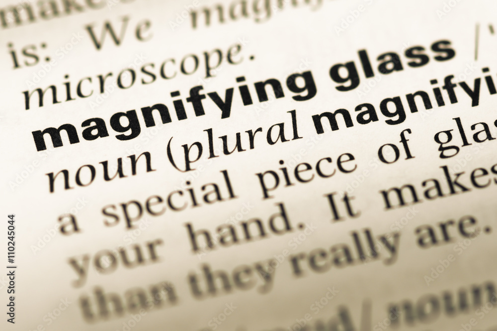 Close up of old English dictionary page with word magnifying gla