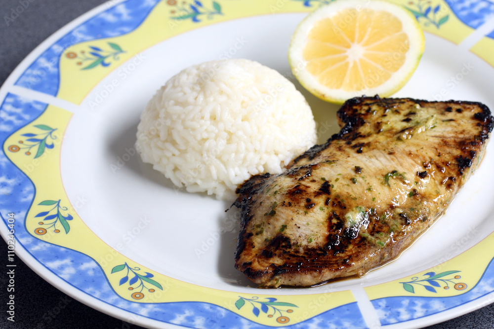 decorated plate with fried fish: tuna filet with rice and lemon, served