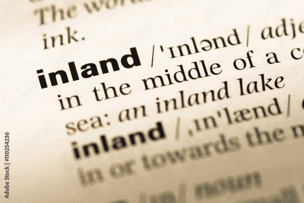 Close up of old English dictionary page with word inland Close up of old English dictionary page with word inland
