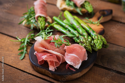 Parma ham, asparagus and arugula on a wooden background