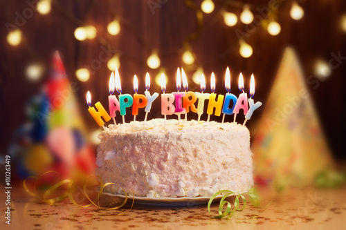 Birthday cake with candles, bright lights bokeh.