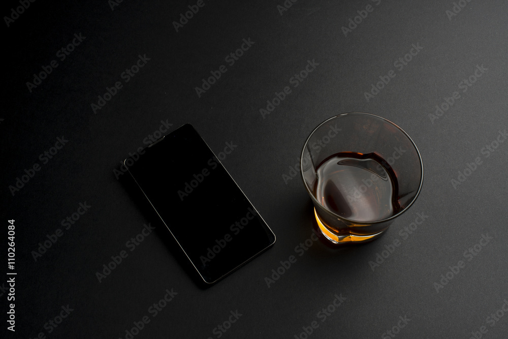 Smartphone and cognac on a black table