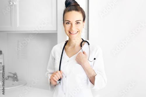 Lekarz pediatra. Młoda uśmiechnięta lekarka w białym kitlu ze stetoskopem.