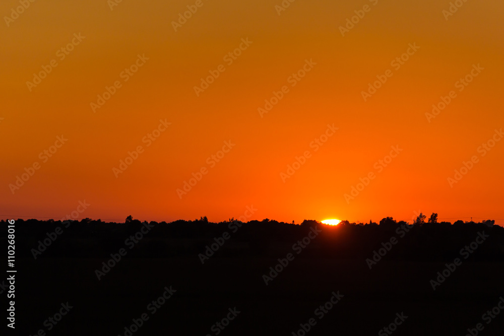 Calm hot sunset on the background of horizontal silhouette forests and villages