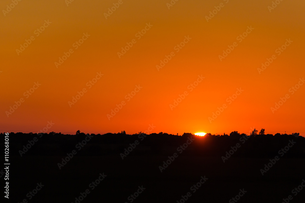 Calm hot sunset on the background of horizontal silhouette forests and villages Calm hot sunset on the background of horizontal silhouette forests and villages
