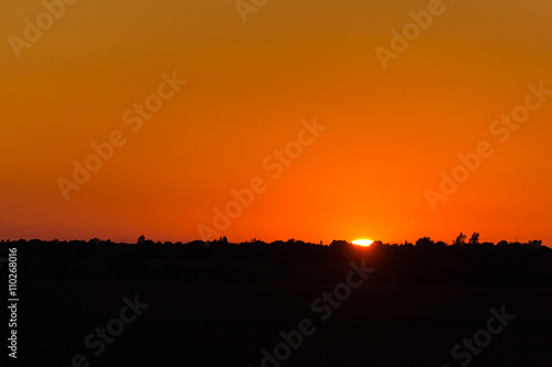 Calm hot sunset on the background of horizontal silhouette forests and villages photo