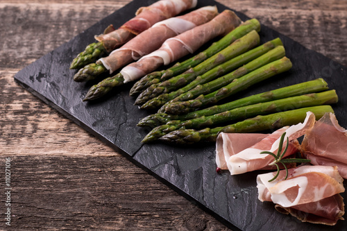 Fresh organic asparagus wrapped in Parma ham on a cutting board