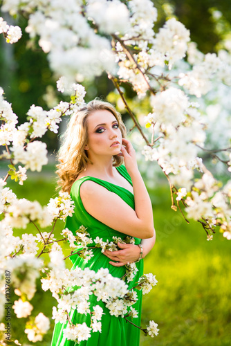 beautiful young blond woman standing beside a blossoming Apple tree