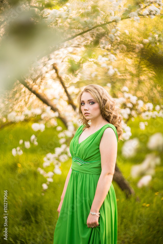 beautiful young blond woman standing beside a blossoming Apple tree