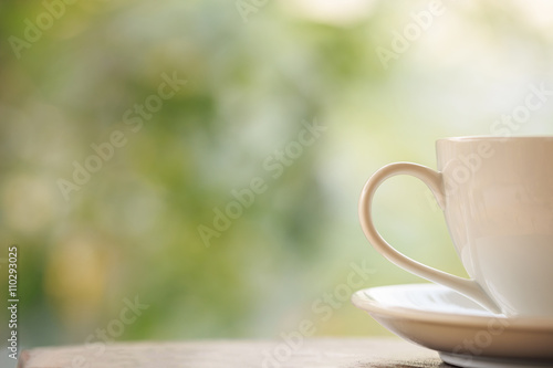 White coffee cup on table in garden with blur light bokeh