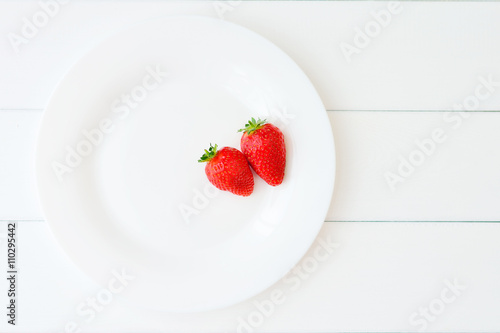 A stack of pancakes with strawberries on a white plate on a wooden white table. Top view 