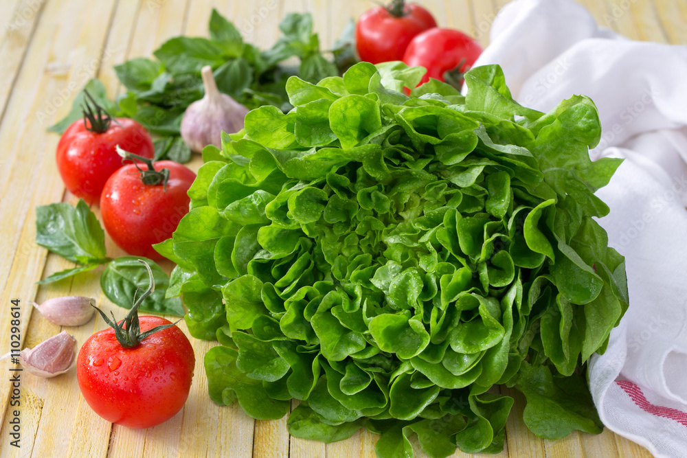 Fresh lettuce, tomato, basil and garlic for a light summer salad on a wooden surface, selective focus Fresh lettuce, tomato, basil and garlic for a light summer salad on a wooden surface, selective focus