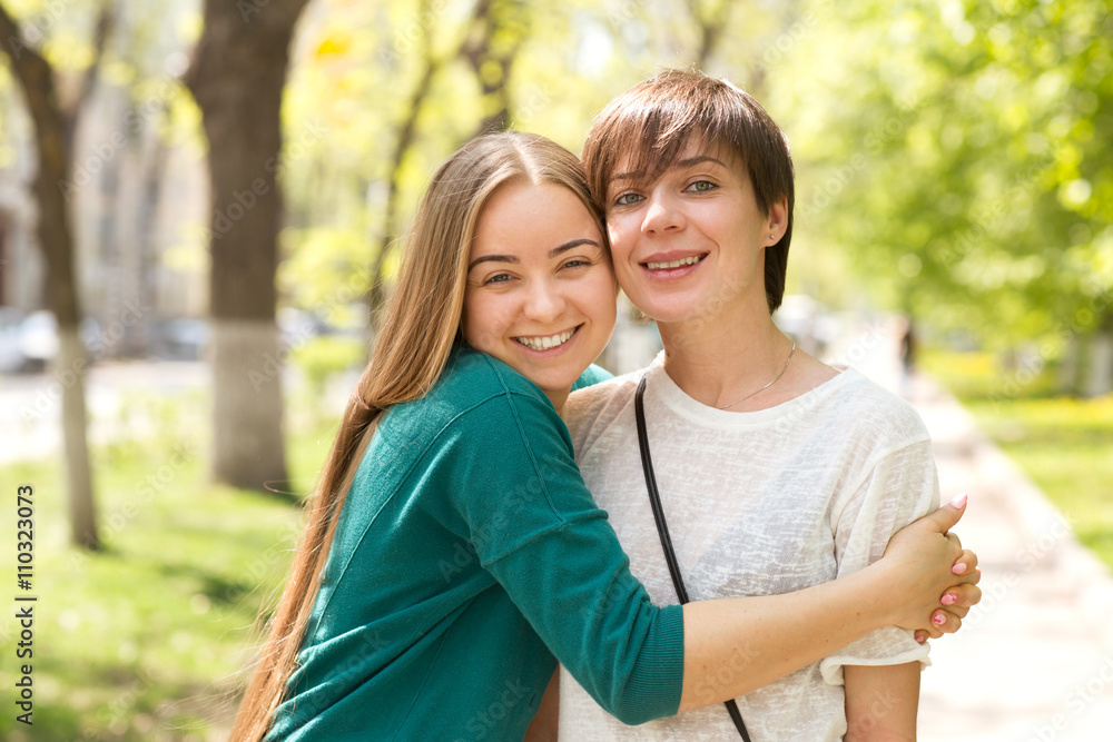 Happy young women friends embracing in green summer garden or park
