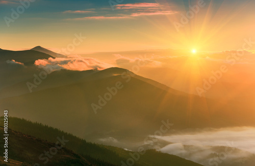 Sunrise landscape of foggy and cloudy mountain valley.