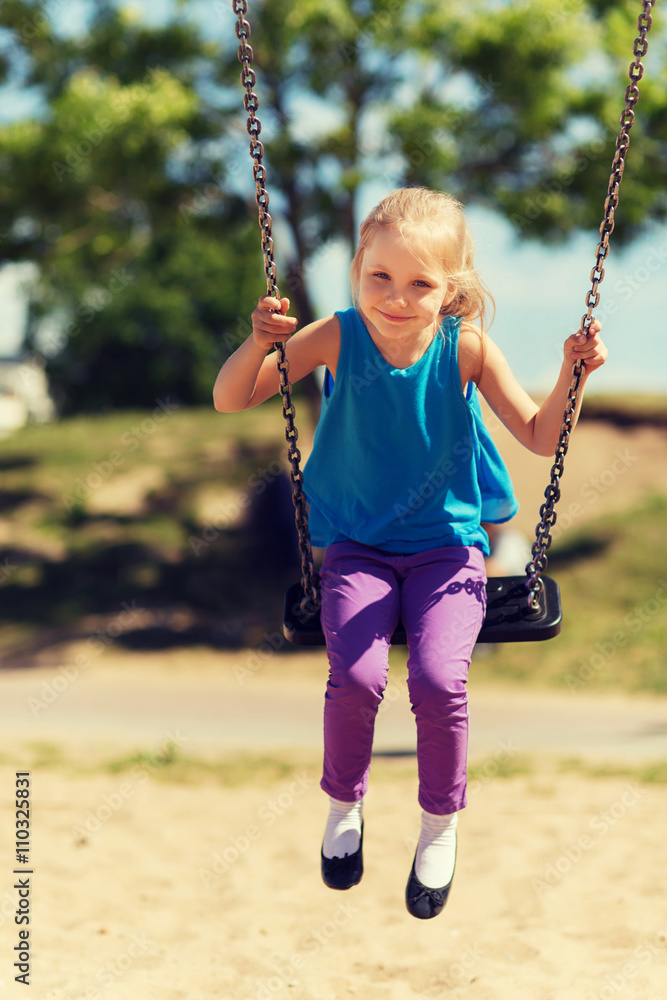happy little girl swinging on swing at playground