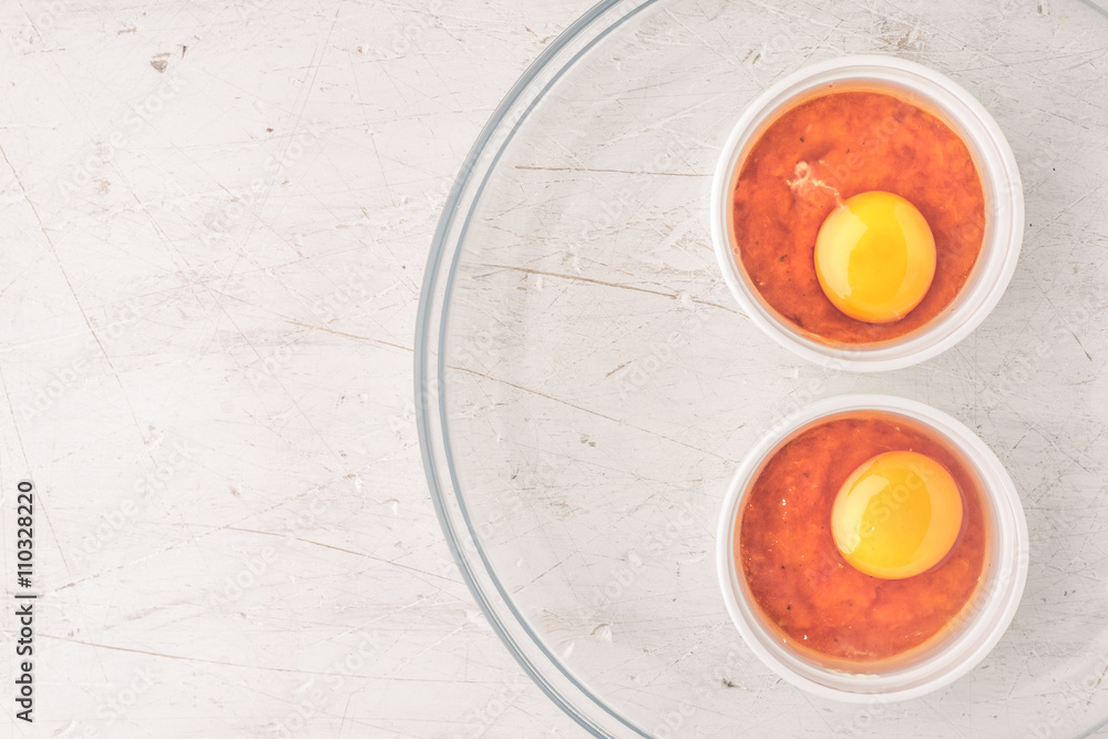 Raw eggs with tomatoes in the ramekins on the white wooden table top view Raw eggs with tomatoes in the ramekins on the white wooden table top view