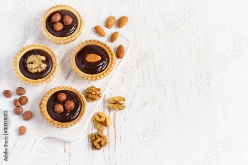 Almond walnut hazelnut chocolate small tarts on a white backgrou © colnihko